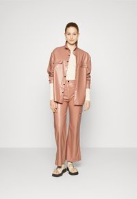 Casaco de pele sintética rosa pálido e calças largas coordenadas com bolsos de carga, combinados com sandálias brancas de tiras e um top texturizado em creme.
