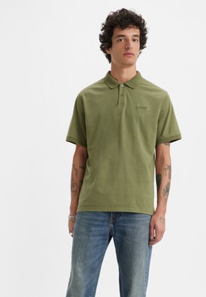 Polo din bumbac verde măsliniu, cu mâneci scurte, închidere cu două butoane și logo brodat. Asortat cu blugi din denim de culoare bleumarin deschis, având o croială relaxată.