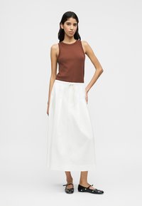 Καφέ αμάνικη μπλούζα, λευκή φούστα μέχρι τους αστραγάλους με κορδόνι στη μέση και μαύρα παπούτσια με κοψίματα. Απλά, λεία υφάσματα.