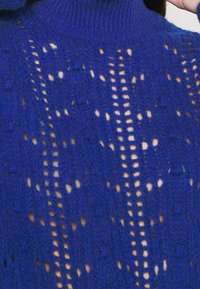 Modrý pletený svetr s texturou a vysokým výstřihem, zdobený otevřenými vzory a kombinací plných a síťovaných částí po celém svetr.