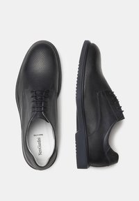 Scarpe in pelle nera con design perforato, chiusura con lacci, suola in gomma e superficie liscia. Presentano una punta leggermente arrotondata e una silhouette elegante.
