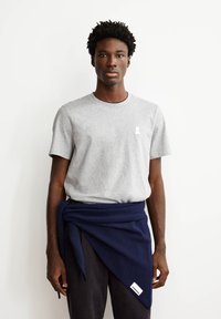 Grijze t-shirt met korte mouwen en ronde hals, met een wit logo op de borst, gecombineerd met een donkerblauwe gebreide sjaal om de taille.