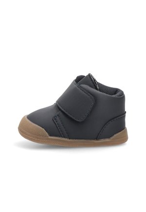 Zapato sintético negro para niños pequeños con una correa de Velcro, suela de goma y puntera redondeada. Cuenta con un forro suave y texturizado para mayor comodidad.