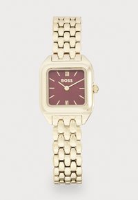 Montre-bracelet en métal doré avec un boîtier carré, un cadran bordeaux, des index d'heure dorés et un bracelet à maillons. Logo présent à 12 heures.