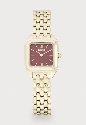 Montre-bracelet en métal doré avec un boîtier carré, un cadran bordeaux, des index d'heure dorés et un bracelet à maillons. Logo présent à 12 heures.