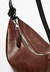 Borsa in pelle marrone con un design elegante, dettaglio della cerniera in argento e una tracolla nera. La texture appare liscia con una leggera lucentezza.