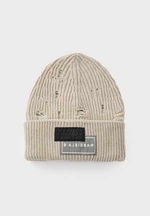Bonnet en tricot beige avec texture côtelée, présentant des détails usés. Comprend une étiquette noire avec des chiffres et le logo de la marque sur le revers.