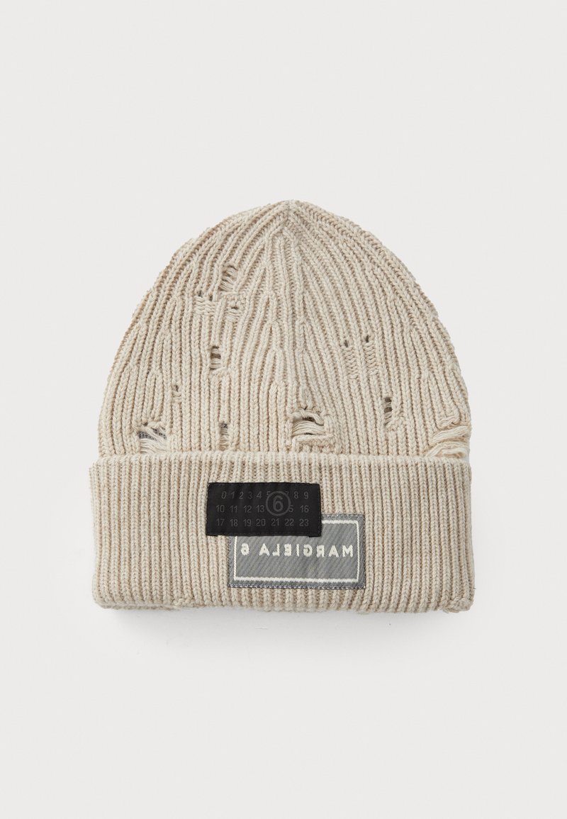 Bonnet en tricot beige avec texture côtelée, présentant des détails usés. Comprend une étiquette noire avec des chiffres et le logo de la marque sur le revers.