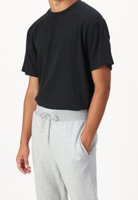 Black short-sleeve t-shirt with embroidered logo, paired with light gray sweatpants featuring an elastic waistband and side pockets.