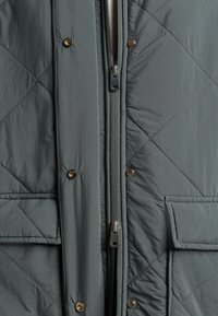 Quilted gray jacket with a front zipper and snap closures. Features two front pockets and a smooth, textured fabric.