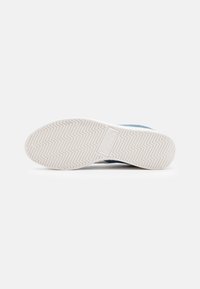 Shoe sole featuring a white rubber base with zigzag tread pattern and blue suede accents on the upper portion for added texture.