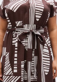 Καφέ φόρεμα με λευκές αφηρημένες ρίγες, με μια ταιριαστή ζώνη δεμένη στη μέση. Ελαφρύ ύφασμα με ρυτιδωτή υφή.