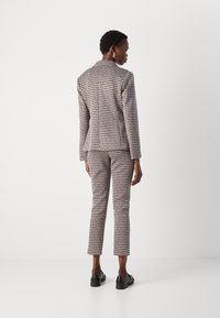 Tailored suit set in textured cream and black pattern, featuring a fitted blazer and slim trousers with a classic cut. Black shoes complete the look.