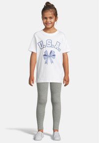 Hvit bomulls t-skjorte med blå "U.S.A." tekst og en sløyfegrafikk, kombinert med grå leggings og hvite sneakers. Enkelt design og passform.