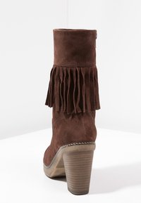 Stivale alto con tacco in camoscio marrone, dettaglio di frange laterali, punta rotonda e tacco impilato testurizzato. Cuciture decorative alla base.