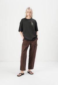 Black oversized t-shirt with an embroidered design on the chest, paired with brown cargo pants featuring multiple pockets and a relaxed fit.