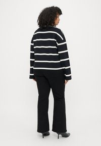 Sort og hvid stribet langærmet top med en afslappet pasform, parret med sorte flagrende bukser og sorte hæle, set fra ryggen.