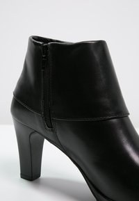Bottine noire à talon haut en cuir lisse avec une fermeture éclair latérale, présentant une silhouette élégante et un design minimaliste sans décorations.
