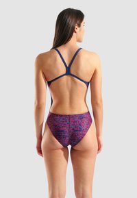 Navyblauwe badpak met een gestructureerd paars en rood patroon. X-back ontwerp en hoge beenopening. Gladde stof met contrasterende accenten.