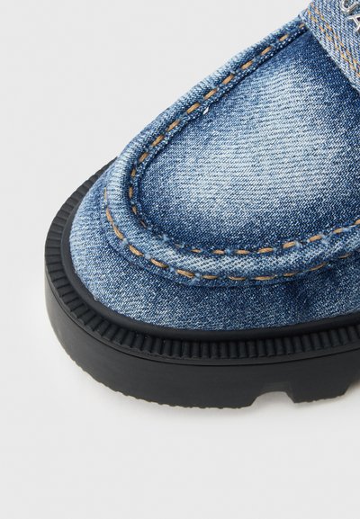 Τζιν μοκασίνι με παχύ μαύρο λαστιχένιο πάτο. Ραφές σε καφέ χρώμα, στρογγυλεμένη μύτη και υφασμάτινο επάνω μέρος από τζιν με υφή.