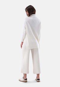 Weißer Strickpullover mit hohem Kragen, kombiniert mit weit geschnittenen weißen Hosen. Das Outfit zeichnet sich durch eine lockere Passform und weichen Stoff aus. Legere Sneakers runden den Look ab.