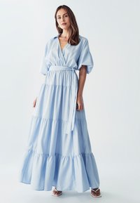 Světle modré vrstvené maxi šaty s V-výstřihem a krátkými nafouklými rukávy. Obsahují textilní pásek v pase a volné lemování.