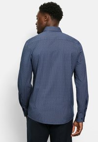 Dunkelblaues Langarmshirt mit kleinem weißen geometrischen Muster, Button-Down-Kragen und strukturierter Stoff. Figurbetonter Schnitt mit knöpfbaren Manschetten.