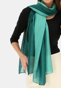 Turkusowy szal wykonany z lekkiej, przezroczystej tkaniny, elegancko ułożony wokół szyi, o gładkiej fakturze i delikatnym połysku.