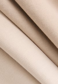 Béžová látka s hladkou štruktúrou, ktorá zobrazuje jemné rebrované vzory a mäkké záhyby, čo naznačuje pružný a ľahký materiál.