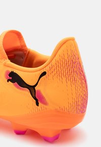 Scarpa da calcio arancione brillante con un design testurizzato, logo Puma nero e tacchetti della suola accentuati in rosa. Materiale sintetico leggero.