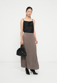 Svart satin cami topp kombinert med en flytende, taupe skjørt; modell som holder en svart samlet veske; iført svarte spissede støvler.