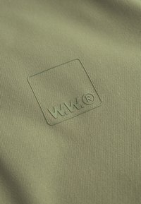Green textured fabric featuring an embossed logo with "W.W." inside a square. The material exhibits fine, vertical ribbing.