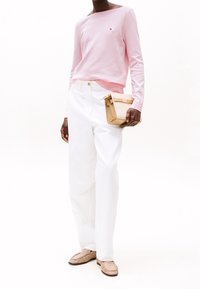 Hellrosa Pullover mit Bootsausschnitt, weiße weit geschnittene Hose und beige Handtasche. Beigefarbene Slipper runden das Outfit ab.