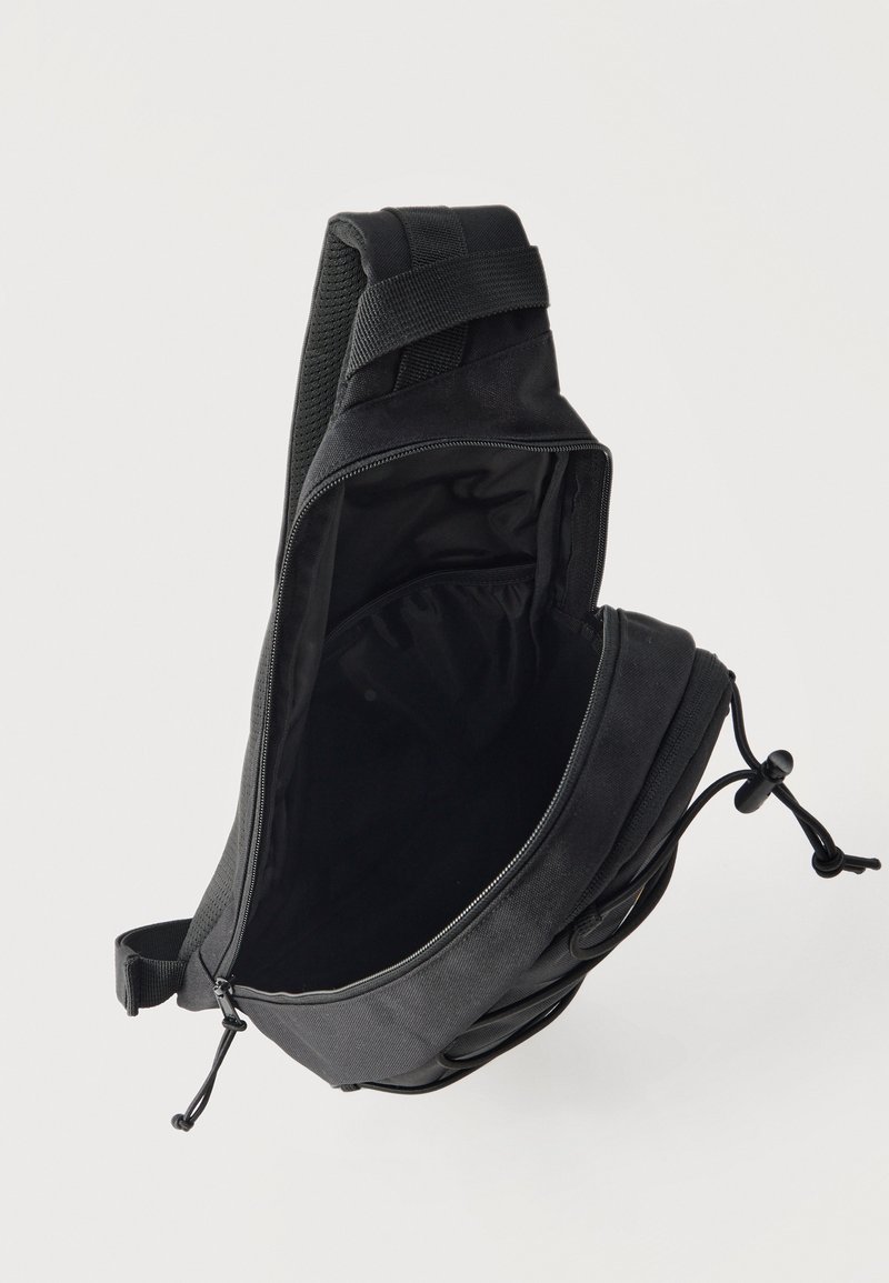 Bolso bandolera negro con compartimento principal abierto y correa ajustable, mostrado sobre un fondo claro y liso.