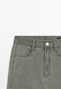 Jean en denim gris délavé taille haute avec bouton à l'avant, passants de ceinture, poches avant visibles et coutures sur fond blanc.
