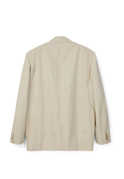 Beżowa marynarka z długimi rękawami, pokryta rozrzuconymi drobnymi czarnymi plamami farby, guziki na mankietach, widoczna od tyłu.