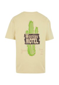 Trumpas rankovės, šviesiai geltonas marškinėliai, pagaminti iš medvilnės. Užpakalyje yra žalias kaktuso grafikas ir tamsiai rudas tekstas "Western Motel".