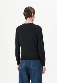 Maglione nero lavorato a maglia con scollo rotondo e maniche lunghe, con vita aderente e polsini a costine, indossato con jeans blu a vita alta.