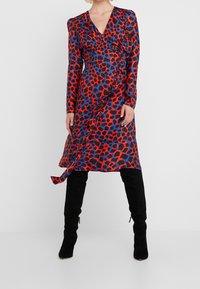 Röd och blå leopardmönstrad klänning med långa ärmar, V-ringning och drapering på sidan. Matchad med knähöga svarta stövlar.