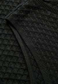 Tissu tricoté noir avec un motif texturé en forme de nid d'abeille et des bords qui se chevauchent, mettant en valeur des détails du matériau doux et dense.