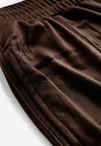 Tejido de terciopelo marrón con una textura suave y un ligero brillo, que presenta una cinturilla elástica fruncida y costuras bien acabadas a lo largo de los bordes.