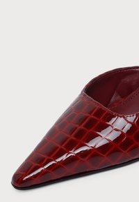 Chaussure pointue rouge foncé brillante avec une texture crocodile et une ouverture latérale basse.