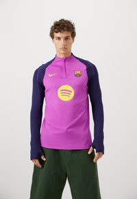 Lilla og marineblå langærmet atletisk top med halvlukning, Barcelona-logo og et stort gult Spotify-emblem på brystet.