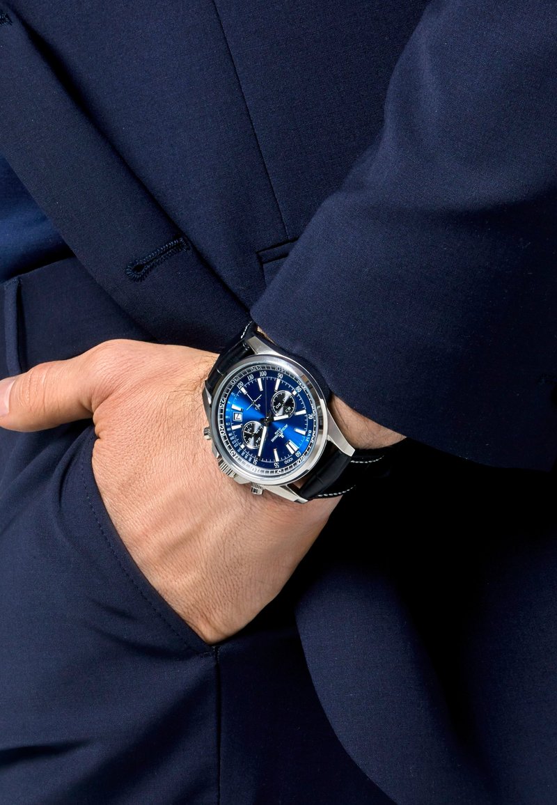 Kronograf klocka med blå urtavla, fodral i rostfritt stål, svart läderrem och silverdetaljer. Har tre subdials och datumdisplay.