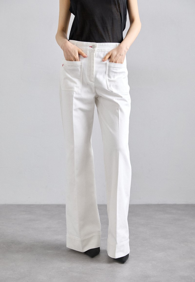 Weiße weit geschnittene Hose mit Fronttaschen, gefertigt aus robustem Stoff. Mit Knopf- und Reißverschluss, klaren Linien und taillierter Passform.
