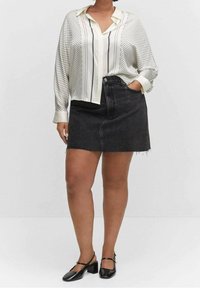 Schwarz-weiß gestreifte Bluse mit langen Ärmeln, kombiniert mit einem hochgeschnittenen Denim-Rock. Das Modell trägt schwarze Lackleder-Blockabsatzschuhe.