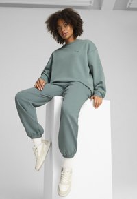 Lys grøn sweatshirt og joggers lavet af blødt stof, med elastiske manchetter. Hvide sneakers med en struktureret detalje er på.