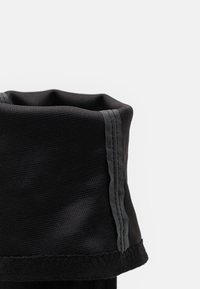 Col montant en polaire noire avec un tissu texturé, présentant des coutures grises le long du bord. Le design est replié pour mettre en valeur le matériau intérieur.