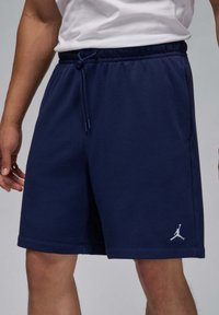 Marineblå sportsshorts lavet af blød stof, med en elastisk talje og justerbar snor samt et hvidt logo på venstre ben.