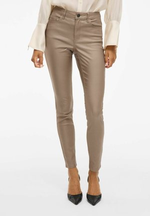Tan slim-fit broek van gladde stof, met vijf zakken, riemlussen en een knoopsluiting. Draag ze met zwarte hoge hakken.